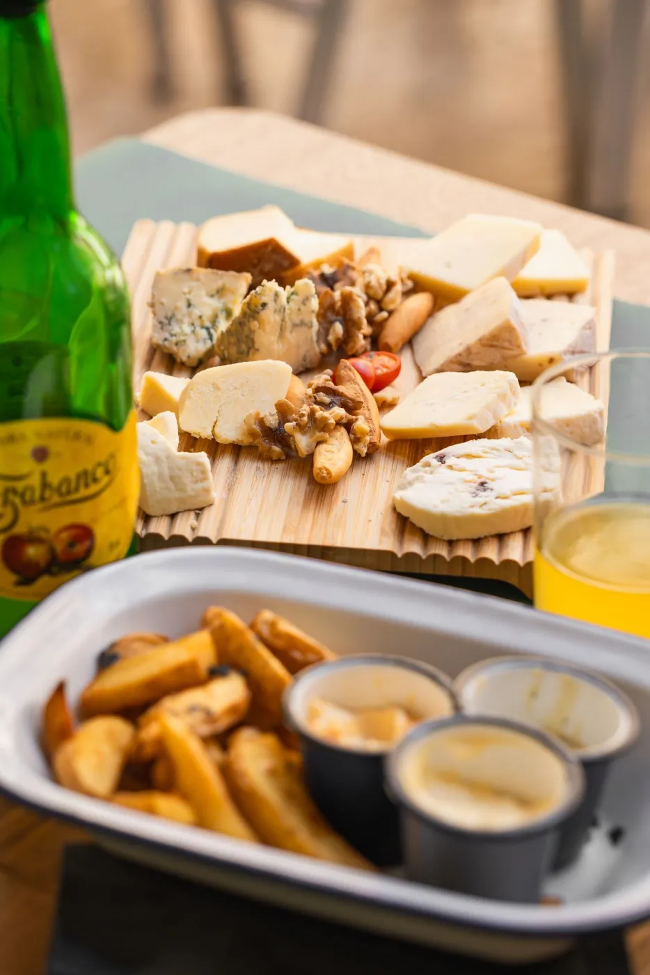 Sidra asturiana Trabanco junto a tabla de quesos y patatas bravas en La Kchoperia