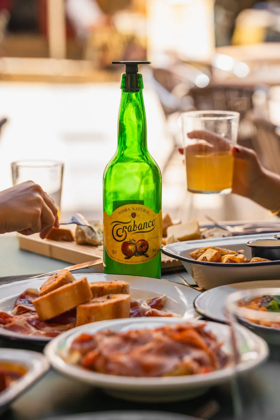 Botella de sidra asturiana y brindis en mesa compartida con luz cálida